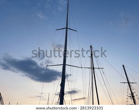 Low angle view of sailboat masts and rigging against a beautiful twilight sky, silhouettes of yacht masts at a marine harbor port during sunset with soft colorful clouds.