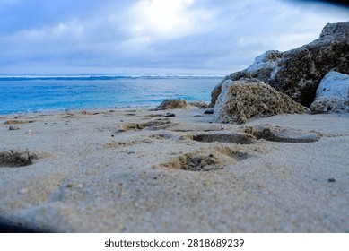Low Angle View of Sandy Beach, Coastal Rocks, and Turquoise Ocean Under Dramatic Cloudy Sky