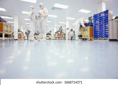 A low angle view of scientists in clean suits discussing a report in the silicon wafer manufacturing laboratory - Powered by Shutterstock