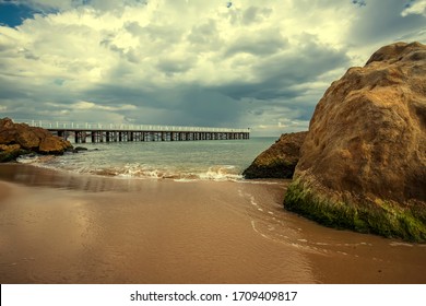 Low angle view of the sea waves with a pier and big rocks on the shore