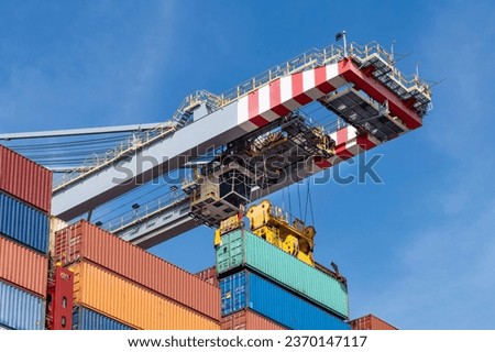 Low angle view of section of stacked sea containers being handled by a gantry crane for ‘ship to shore’ in container terminal against a blue sky