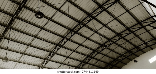 Low angle view of a semi open hall building showcasing ceiling framework, roof structure, and airy architectural layout. Natural lighting enhances the structural details and symmetry, creating a bright and spacious atmosphere. Suitable for concepts such as modern architecture, construction, public facility, industrial design, and urban development.
