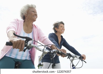 Low Angle View Of Senior Female Friends Riding Bicycle Against Sky