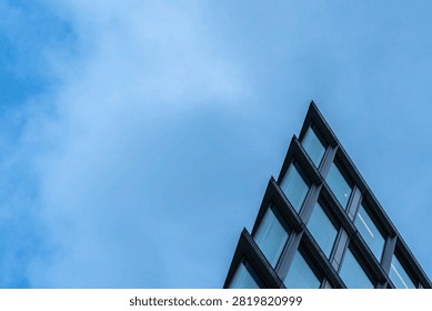 Low angle view of the sharp stepped corner of a modern glass office building against a blue cloudy sky, creating a minimalist architectural composition with copy space
