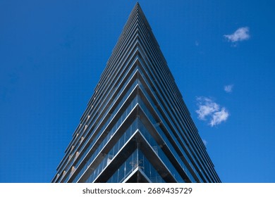 Low angle view of sharp-angled building against blue sky with small fluffy clouds
