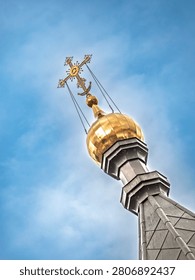 Low angle view of a shiny gold dome and ornate cross on an Orthodox cathedral spire. Represents faith and Eastern European architectural heritage under a cloudy sky.