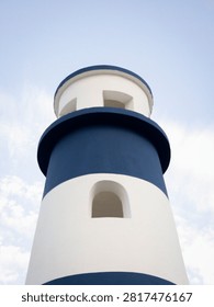 A low angle view shows a blue and white striped lighthouse structure. The lighthouse stands tall against a clear sky, highlighting its features. This scene captures the essence of coastal design.