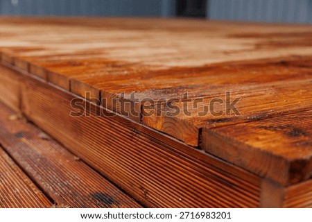 Low angle view shows reddish brown planks, end grain, sawdust, and slight gaps. Joinery and step edge stand out on a residential deck in soft daylight.