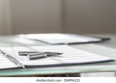 Low Angle View Of Silver Ink Pen Lying On White Sheet Of Paper In A Folder With Another Set Of Paperwork At The Opposite Side Of The Desk.