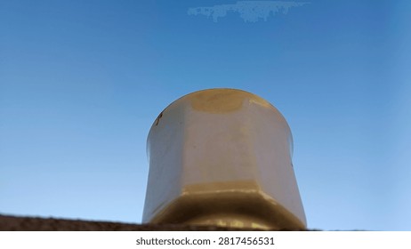 Low angle view of a simple rustic cup resting on a wall ledge against a clear bright blue sky background with massive empty copy space.