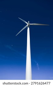 Low angle view of a single white wind turbine against a deep blue sky, representing clean industrial power and renewable energy generation.