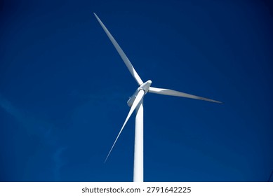 Low angle view of a single white wind turbine against a deep blue sky, representing clean industrial power and renewable energy generation