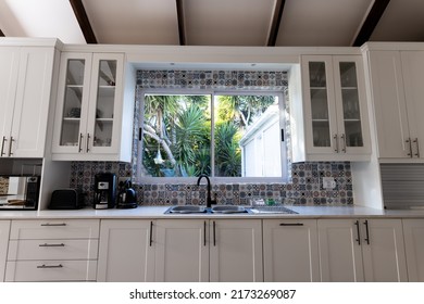 Low angle view of sink, window and closed white cabinets in modern kitchen, copy space. Kitchen counter, unaltered, furniture, home and interior decoration concept.