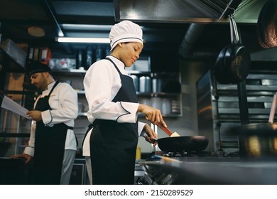 Low angle view of smiling African American woman cooking while working as chef in a restaurant.  - Powered by Shutterstock