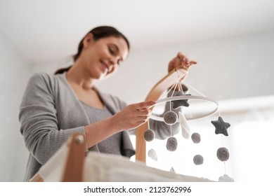 Low angle view of smiling caucasian woman installing a baby mobile toy over the baby's crib - Powered by Shutterstock