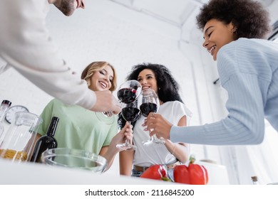 low angle view of smiling multiethnic friends clinking glasses of red wine in kitchen - Powered by Shutterstock