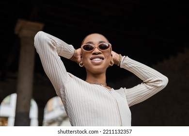 Low Angle View Of Smiling Short Haired African American Woman In Sunglasses Standing Outdoors