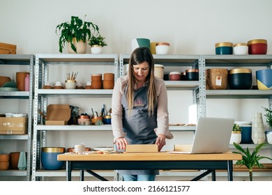 Low Angle View Of Smiling Woman In Apron Preparing Christmas Ornaments Of Clay For Delivery At Her Store