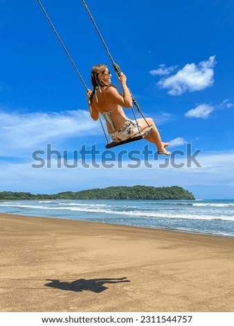 LOW ANGLE VIEW: Smiling young lady enjoying on a beach swing at Playa Venao. She is having a carefree summer moment at beautiful ocean beach in Panama. A paradise location for a tropical holiday.