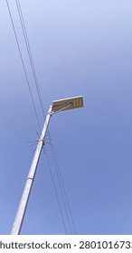 Low angle view of a solar powered street light pole with electric cables under a bright blue sky.