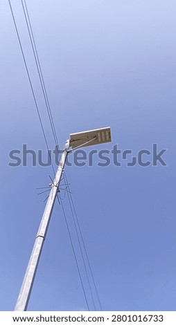 Low angle view of a solar powered street light pole with electric cables under a bright blue sky.