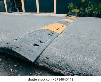 Low angle view of a speed bump installed on an asphalt road with yellow and black warning markings. Traffic calming device designed to slow down vehicles and improve road safety in urban, residential, or parking area environments. Suitable for transportation, infrastructure, safety, and urban street concepts.