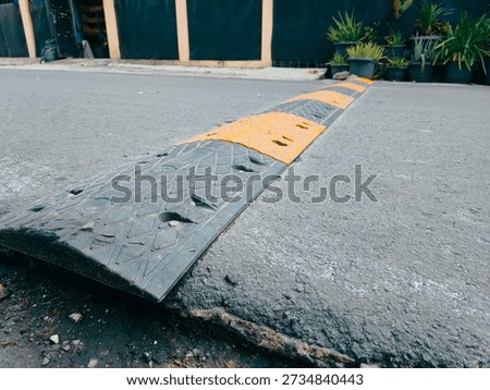 Low angle view of a speed bump installed on an asphalt road with yellow and black warning markings. Traffic calming device designed to slow down vehicles and improve road safety in urban, residential, or parking area environments. Suitable for transportation, infrastructure, safety, and urban street concepts.