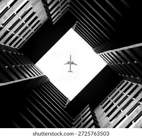 Low angle view of a square building courtyard silhouette with an airplane flying in the bright sky center, geometric architectural fine art photography