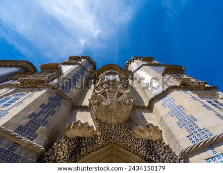 Low angle view of the Statue of Triton on a shell with decorative stone carving that guards the entrance to the Pena Palace, with the towers decorated with Portuguese mosaics. Sintra. Portugal.