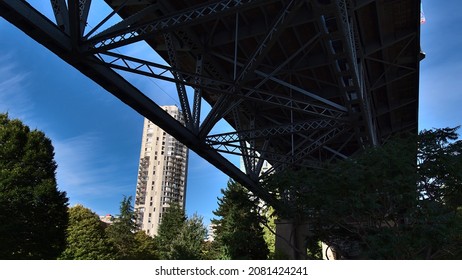 Low angle view of steel truss bridge Burrard Street Bridge, spanning False Creek and connecting Kitsilano with Vancouver downtown in British Columbia, Canada, with trees and residential building.