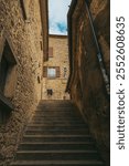 Low angle view of a stone stairway ascending between weathered stone buildings in a narrow alleyway of san marino, featuring brown shutters, a glimpse of the sky, and a sense of historical charm