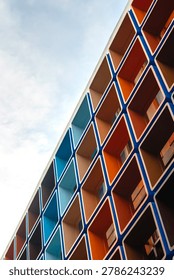 Low angle view of a striking geometric building exterior. The modern facade displays a repeating grid pattern of vivid blue and orange square panels against a bright sky. A contemporary design.