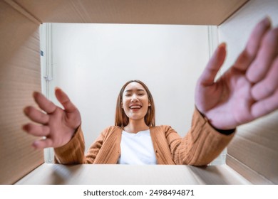 Low angle view of surprised young asian woman unpacking. Opening carton box and looking inside. Packaging box, delivery service. Human emotions and facial expression - Powered by Shutterstock