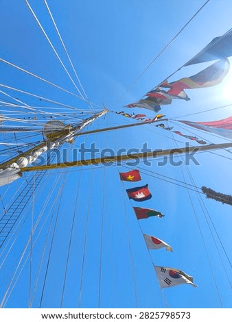Low angle view of a tall ship mast and complex rope rigging decorated with colorful international national flags against a clear bright blue sky in Bitung, Manado, Indonesia.