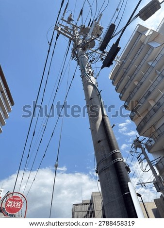 Low angle view of a tall utility pole with complex power lines between modern buildings under a blue sky in Japan.