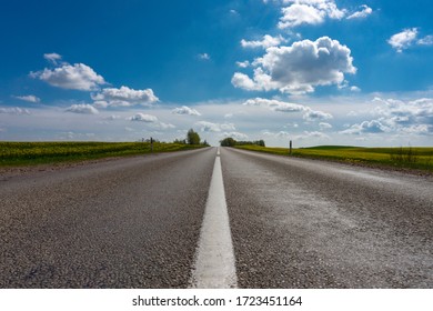 Low Angle View Of A Tarred Road Receding Into The Distance In Open Countryside Under A Cloudy Blue Sky With Focus To The Center White Line