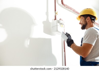 Low angle view of technician, heating fitter in hard hat and protective gloves making notes while checking gas consumption at gas pipe and meter counter