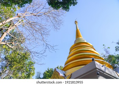 Low angle view of Thai golden pagoda in buddhist temple against clear blue sky with trees branches and green leaves around - Powered by Shutterstock