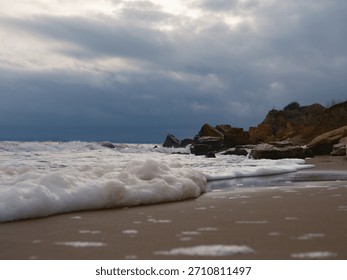 Low angle view of thick white sea foam on wet sandy beach. Black Sea coast, stormy weather, dramatic dark cloudy sky, autumn atmosphere, raw nature background