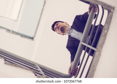 Low angle view of thinking businessman leaning on railings and looking straight. Pensive young man contemplating in stairwell. Business concept - Powered by Shutterstock