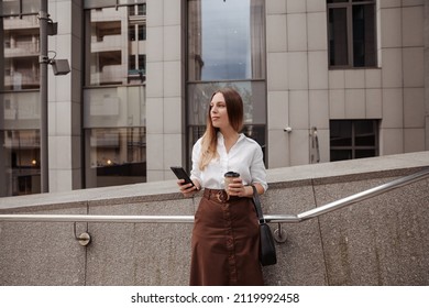 low angle view of thoughtful young businesswoman looking at smartphone on city street