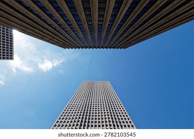Low angle view of three modern geometric skyscrapers against a vibrant blue sky with scattered clouds.