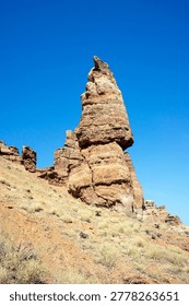 Low angle view of a towering vertical sandstone rock formation resembling a castle spire against a clear blue sky in Charyn Canyon Kazakhstan