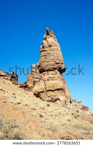 Low angle view of a towering vertical sandstone rock formation resembling a castle spire against a clear blue sky in Charyn Canyon Kazakhstan