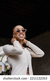 Low Angle View Of Trendy African American Woman In Sunglasses Smiling On Urban Street