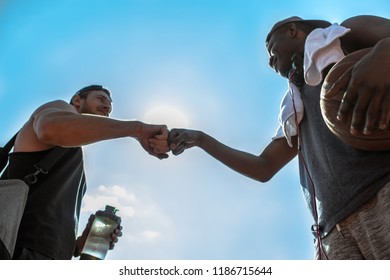Low angle view of two basketball players fistbumping against blue sky after match in outdoor court, copy space