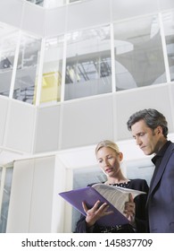 Low Angle View Of Two Business People Looking At Folder In Office Atrium