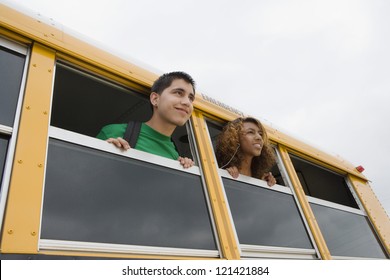 Low angle view of two happy students looking through window of a school bus