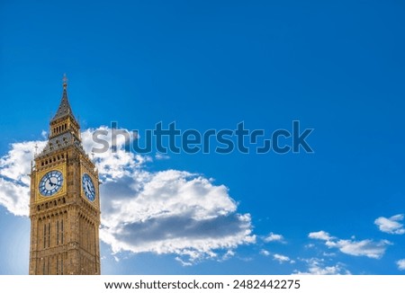 Low angle view of two sides of the Big Ben Clock Tower seen in great detail of its gold ornamentation and cross capital on a bright day with clear blue sky and backlit clouds with plenty of copy space