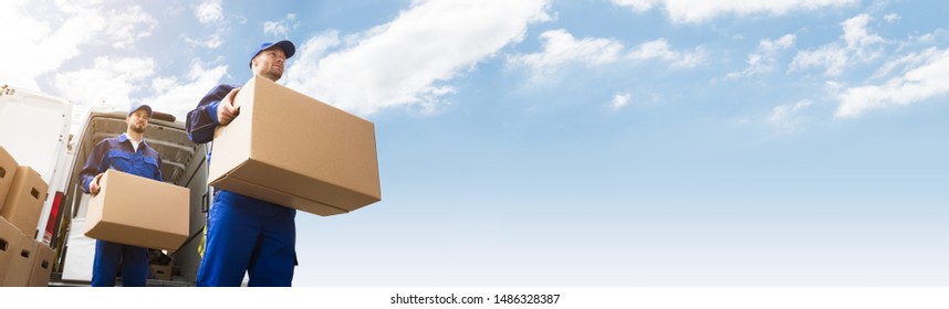 Low Angle View Of Two Young Delivery Man Carrying Cardboard Box In Front Of Truck